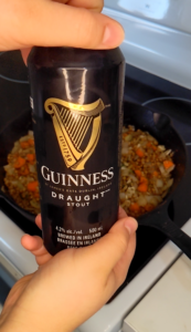 Front and focal image of a can of Guinness Stout beer. The can is being opened. 