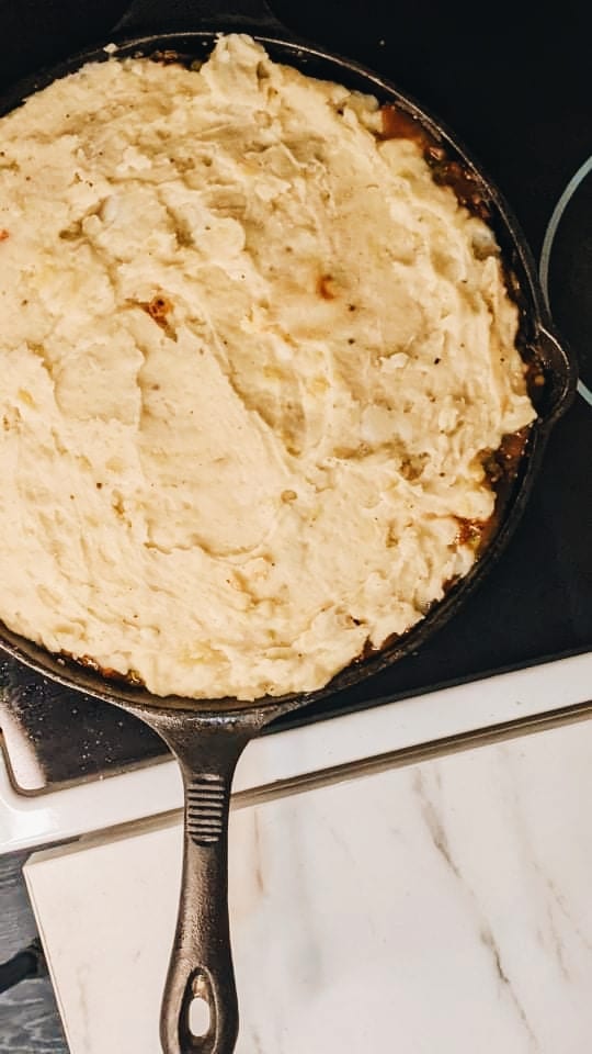 A heavy cast iron pan, filled with lentil and vegetable gravy, topped with fluffy mashed potatoes. Waiting to be baked in the oven for our Guinness and Lentil Shepherd's pie