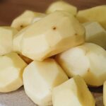 Peeled and halved yukon gold potatoes resting on a cutting board to be cooked momentarily 