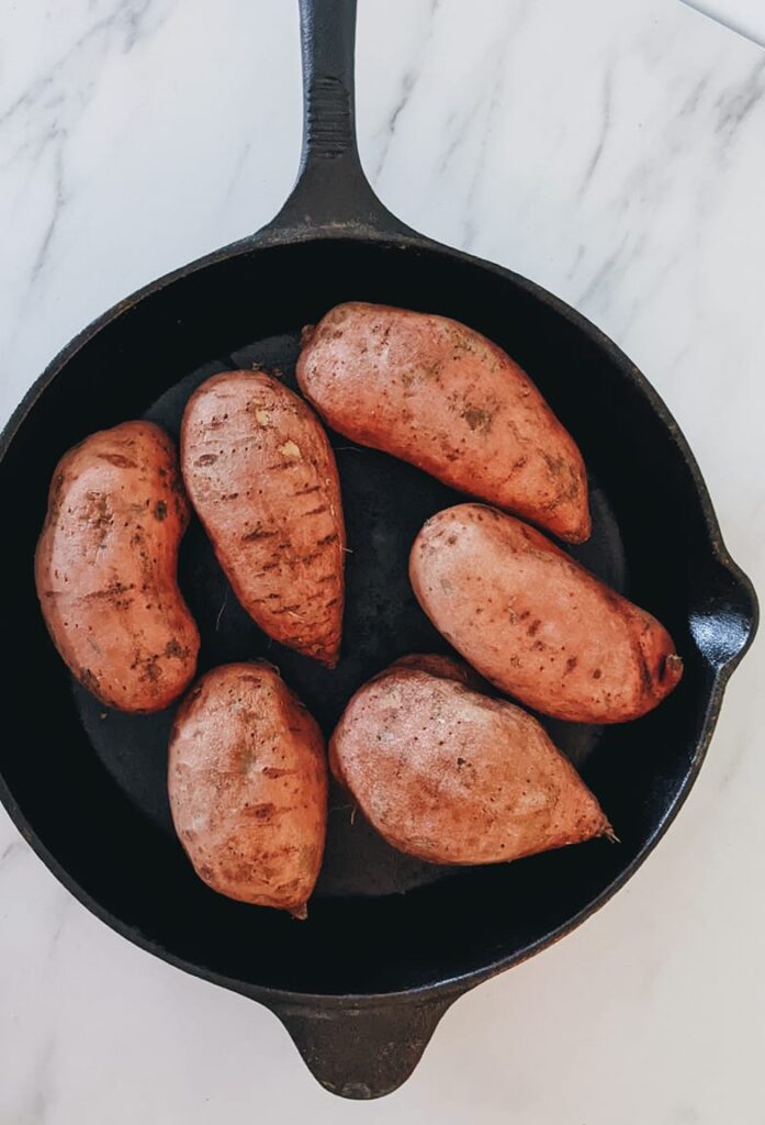 Six washed and uncooked sweet potatoes sitting in a large cast iron pan